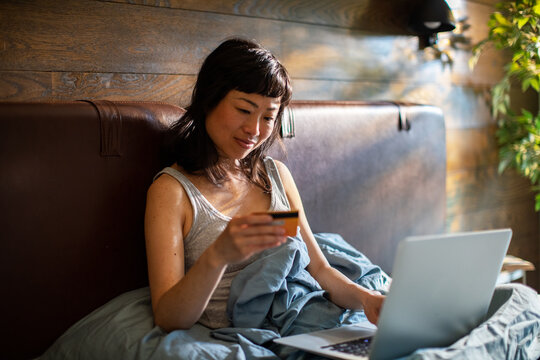 Woman shopping online with credit card in bed at home