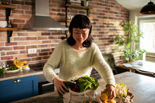 Smiling woman unpacking fresh groceries in home kitchen