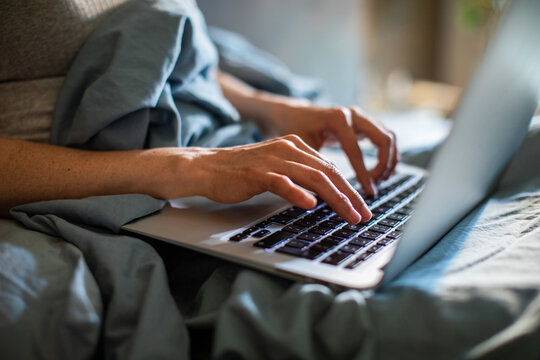 Person working on laptop in bed at home