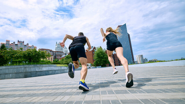 Low angle back view of running couple on urban route. Concept of speed and motion, city running challenge, marathon preparation, and outdoor performance training.