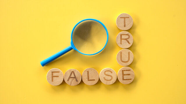 A blue magnifying glass points towards wooden tile blocks spelling out the words True and False, forming an L-shape on a yellow surface.