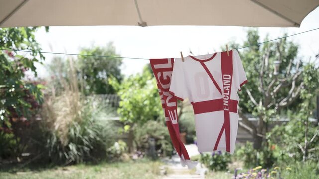 English soccer fan t-shirt and scarf hanging in the wind in garden, background blurred
