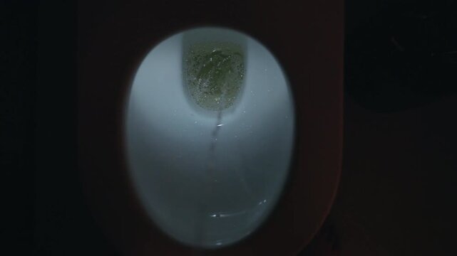 Direct vertical perspective of urination process showing yellow fluid creating foam and bubbles inside a white porcelain plumbing fixture, slow motion