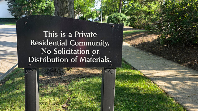 private residential community and no solicitation of materials sign outside by sidewalk with trees and bushes in background during daytime