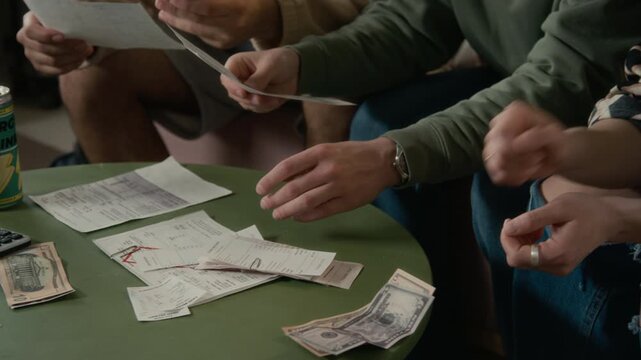 Multiethnic young adults sitting together, counting dollar bills and reviewing past due bills on table. Clip is perfect for marketing financial planning apps, student loan services, or debt relief