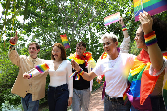 Gathering gay men transgender women and lesbians carrying rainbow flags celebrate the pride and joy LGBTQ community and their gender identities marching parade demand equal rights.