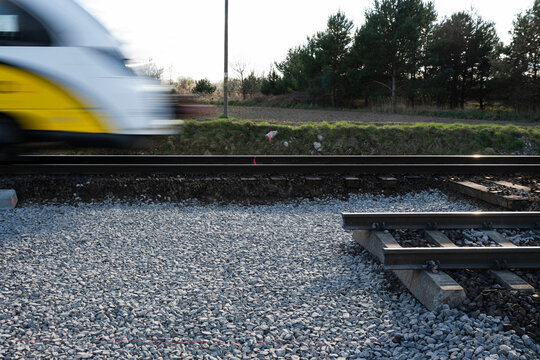A modern yellow and white train passing by at high speed, blurred by motion, next to a railway track construction site with fresh gravel.