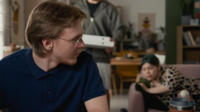 Diverse young adults counting money and sharing pizza costs in living room of shared house, representing student budget struggles. Financial literacy campaigns or banking app advertisements