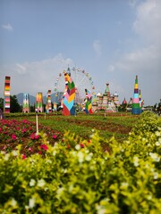 Beautiful colorful theme park landscape with a large ferris wheel, colorful towers, flower gardens, and green mountains under a bright blue sky. Jans Park, Jatinangor, Indonesia. © EkoPriyatno