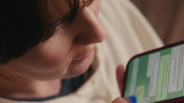 Woman sitting on a sofa using a smartphone to record a voice message in a messaging app. Modern communication and lifestyle concept. High quality 4k footage