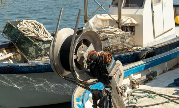 Rusty metal winch reel and wire mesh traps on a commercial fishing vessel in a busy harbor