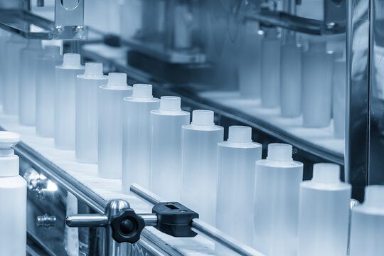 Row of liquid cosmetics bottles moving along a conveyor belt in an automated production line.
