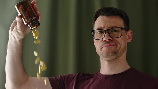 Skeptical man pours capsules from amber supplement bottle indoors during health product review and safety concern concept
