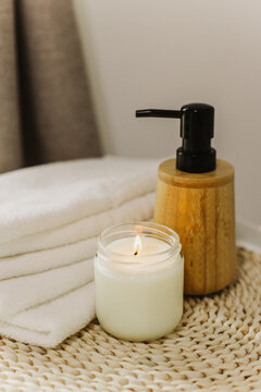 Minimalist still life of luxury spa essentials. White cotton towels with visible textured, bottle with oil and soy wax candle.