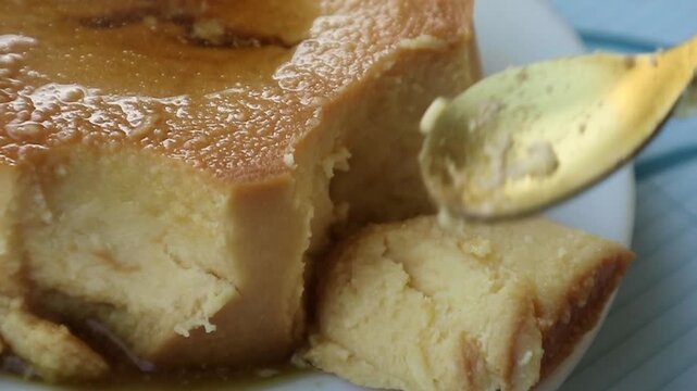 Video of a pudding that has many cuts on each side and is cut using a gold spoon on a white plate.