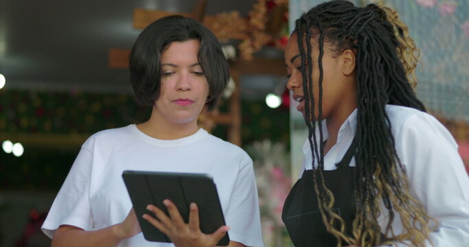 Co workers reviewing inventory or orders on tablet while exchanging ideas outside floral shop, focused on efficient business operations
