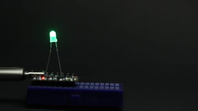 Green color LED diode illuminating light controlled by a micro controller connected to the breadboard on a black background