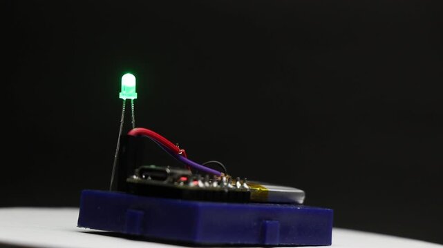 Small lithium polymer battery powering a microcontroller that controls a blinking green LED on a rotating display