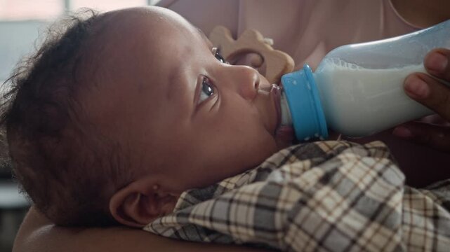 African American infant drinking milk from bottle held by mother in close-up shot. Ideal for baby formula advertisements, parenting blogs and work-life balance
