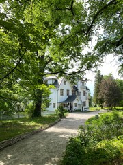Path leading to a historic white house surrounded by lush green trees on a sunny day © dvoevnore
