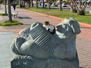 Cat resting on stone sculpture of reclining figure in urban park setting with trees © dvoevnore