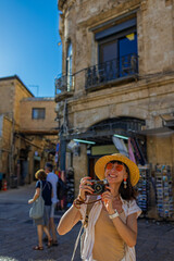 Obraz premium A young woman strolls through Jerusalem with a camera. The girl is smiling and holding a camera. Traveling in Israel.