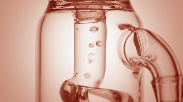 Extreme close of clean colorless liquid flowing through a glass tube, causing bubbles to condense and chaotically move inside it isolated on round beige platform