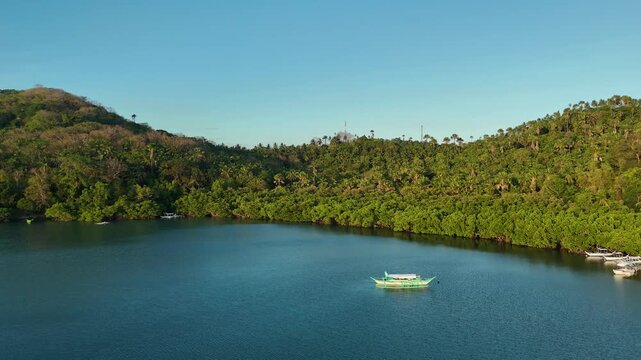 Traditional bangka boat floating on calm blue water near green Mindoro hills