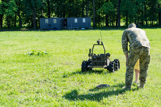 Military Officer Demonstrates Remote Controlled Tracked Unmanned Ground Vehicle On Green Grass Field. Demining of the land on the agricultural field. The sapper is working. Back view of a man