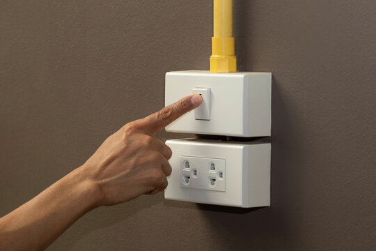 Hand turning on light switch on brown wall