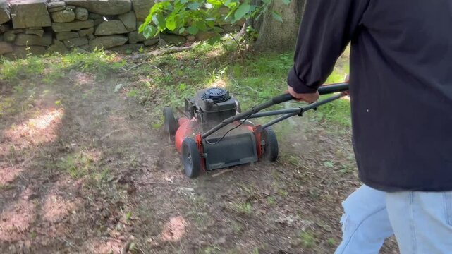 Rear view tracking shot of person mowing patchy backyard dirt
