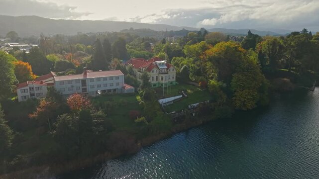 Aerial view establishing dolly in of Teja Island, with wooden architecture and autumn foliage, Maurice van de Maele Historical and Anthropological Museum Valdivia, Chile