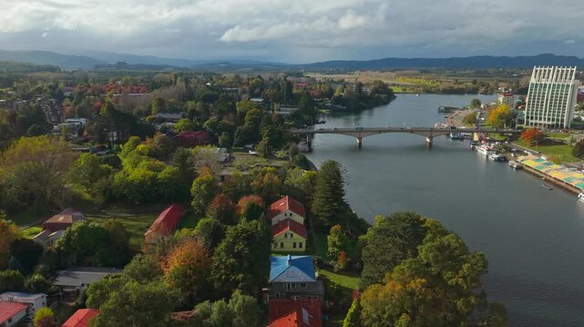 Aerial orbit of Teja Island revealing the city of Valdivia on the Calle Calle River on a sunny day with clouds in the background, Chile