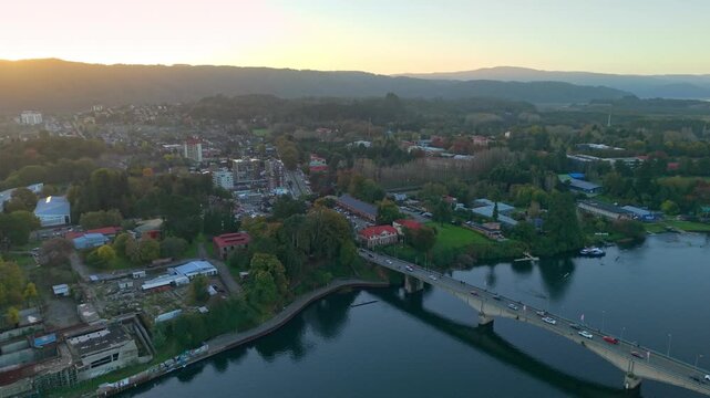 Aerial view dolly in of Teja Island and the Pedro de Valdivia Bridge in Chile at sunrise, with the mountains in the background