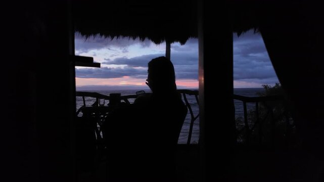 Silhouette of woman watching dramatic tropical sunset from beachside balcony