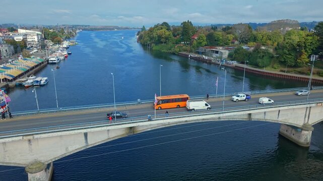 Aerial view dolly in of people walking across the Pedro de Valdivia Bridge and the Calle Calle River, with Teja Island in the background, on a sunny day in Chile