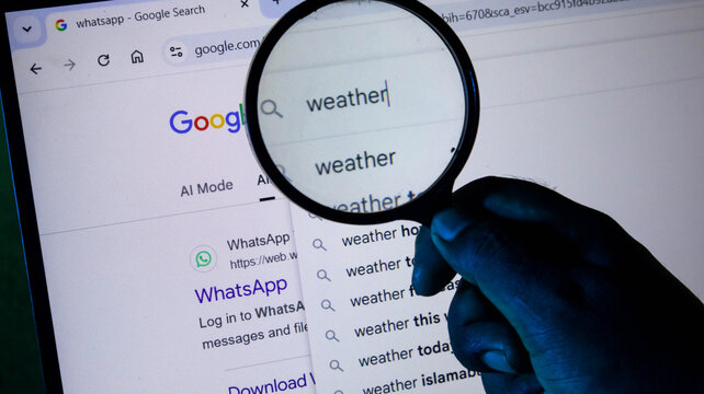 A person using a magnifying glass to search for weather on a computer screen, showing a google search bar with search suggestions