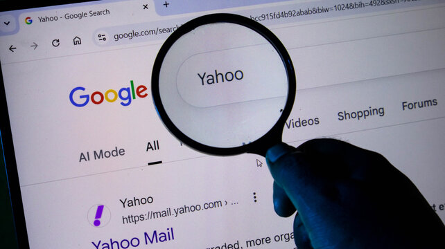 A person using a magnifying glass to look at a yahoo search result on a computer screen displaying a google search page