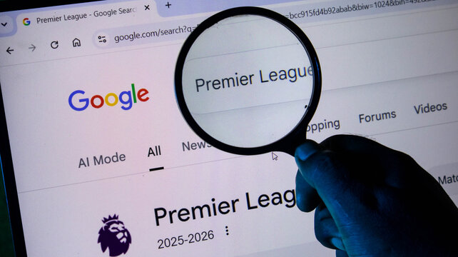 A person holding a magnifying glass over a computer screen displaying a google search result for the premier league football competition