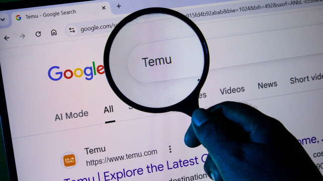 A hand holding a magnifying glass over a computer screen displaying a google search for temu