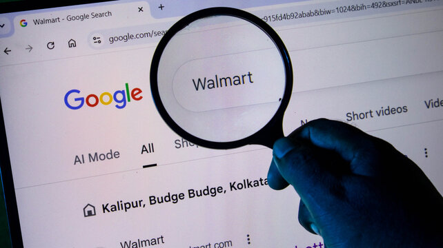 A person holding a magnifying glass over a computer screen displaying a google search for walmart