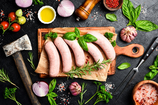 Raw chicken sausages with rosemary and spices, ready to be grilled. On a wooden cutting board. Close up.