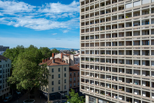 Apartment building stands above urban trees near a residential block, with sky over windows, balcony lines, neighborhood architecture and city scale
