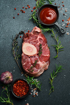 Raw ossobuco steak with rosemary and spices on a black stone background. Free space for text.