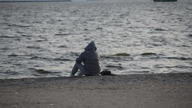 A man alone at the beach in deep thoughts. Spending time alone in contemplation. Dealing with depression. Time at the beach enjoying the view of the ocean, feeling the breeze, and the white sand.