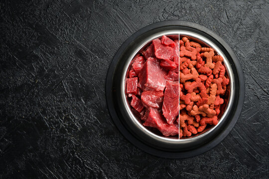 Bowl with food for dogs or cats. Fresh beef and dry fodder. On a black stone background.