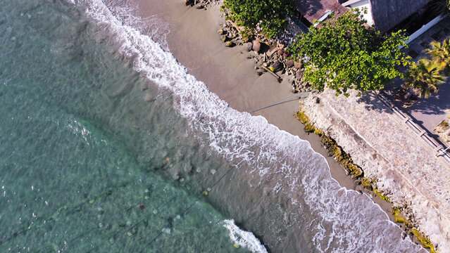 A high-angle drone shot of a shoreline where clear emerald water meets the coastal resort property