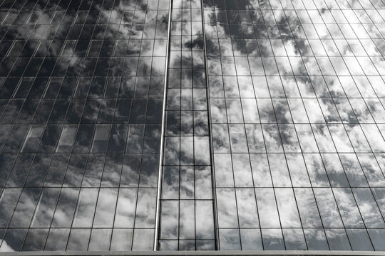 Clouds move across a glass facade in reflection, where a dark grid of windows turns building surface into abstract urban architecture
