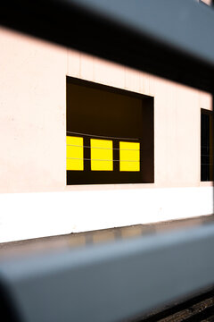Recessed yellow windows sit within a pale facade, where shadow, wall, railing blur and building detail create architectural contrast