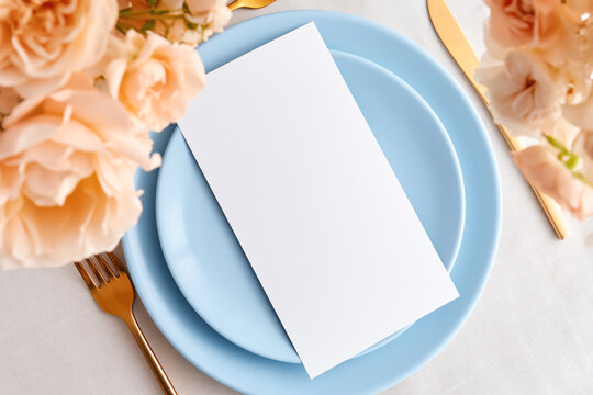 Blank menu card mockup placed on a blue plate with elegant tableware and floral decoration